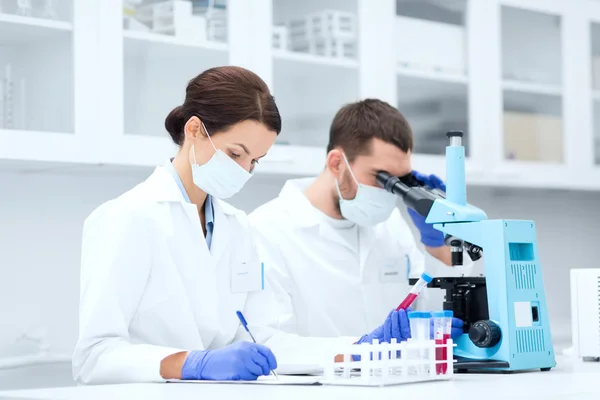 Wetenschappers met Klembord en Microscoop in lab — Stockfoto