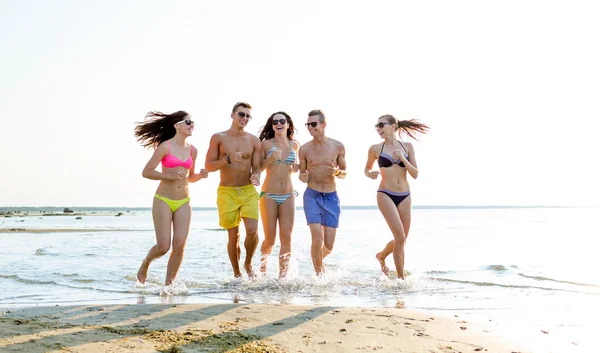 Amigos sorridentes em óculos de sol correndo na praia — Fotografia de Stock