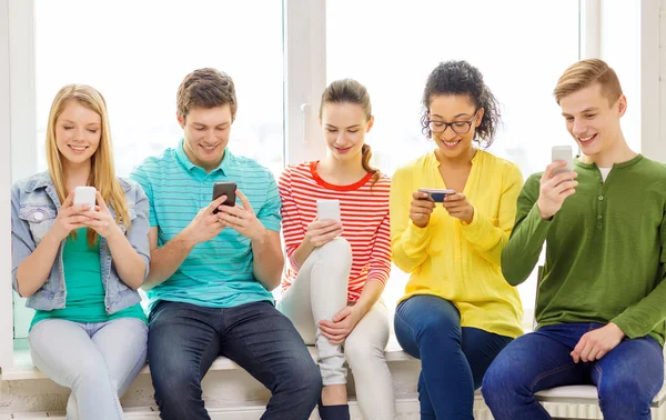 Smiling students with smartphone texting at school — Stock Photo, Image
