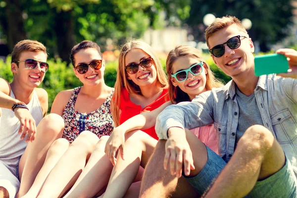 Smiling friends with smartphone sitting on grass — Stock Photo, Image