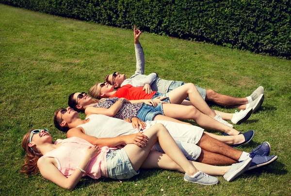 Groep lachende vrienden liggen op gras buitenshuis — Stockfoto