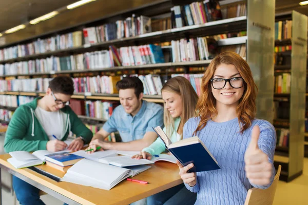 Menina estudante feliz mostrando polegares para cima na biblioteca — Fotografia de Stock