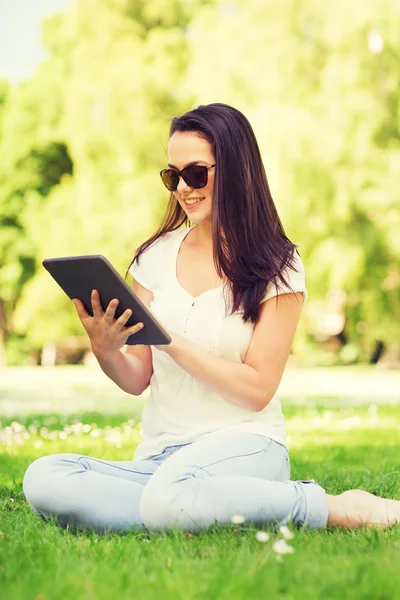 Sonriente chica joven con tableta pc sentado en la hierba — Foto de Stock