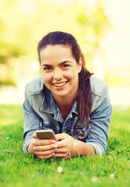 Glimlachend jong meisje met smartphone liggen op gras — Stockfoto