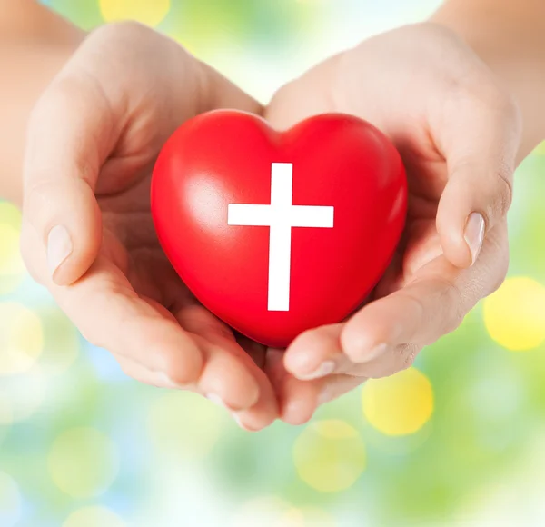 Close up of hands holding heart with cross symbol — Stock Photo, Image