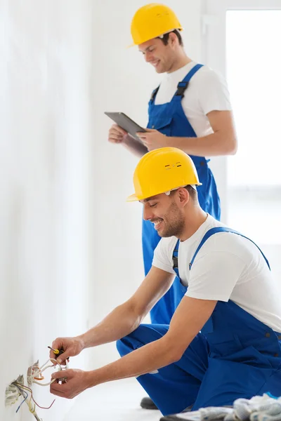Builders with tablet pc and fixing wiring indoors — Stock Photo, Image