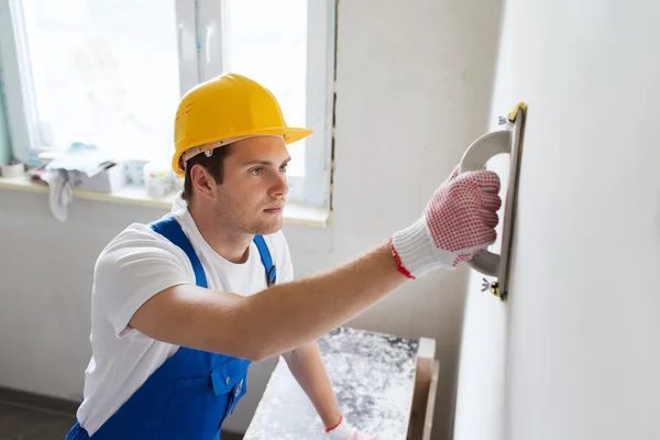 Construtor sorrindo com ferramenta de moagem dentro de casa Imagem De Stock