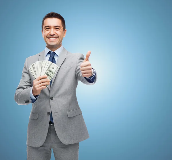 Homem de negócios sorridente com dinheiro mostrando polegares para cima — Fotografia de Stock