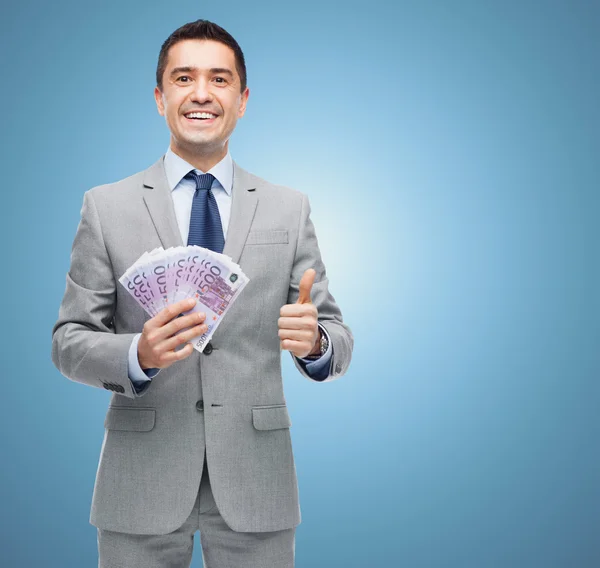 Homem de negócios sorridente com dinheiro mostrando polegares para cima — Fotografia de Stock