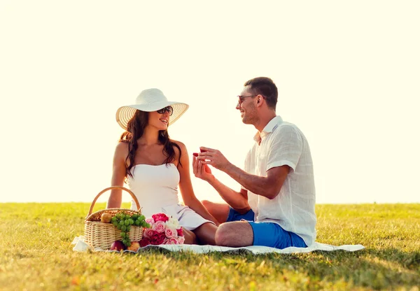 Sonriente pareja con pequeña caja de regalo roja en el picnic — Foto de Stock