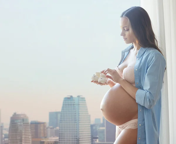 Ευτυχισμένη έγκυος γυναίκα με κοριστίστικα παπουτσάκια στο σπίτι — Φωτογραφία Αρχείου