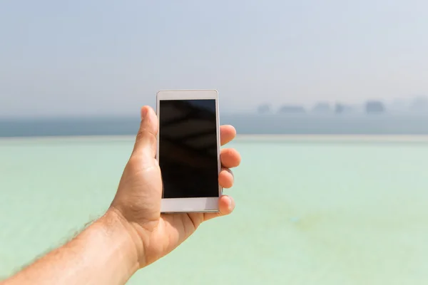 Nahaufnahme einer männlichen Hand, die ihr Smartphone am Strand hält — Stockfoto
