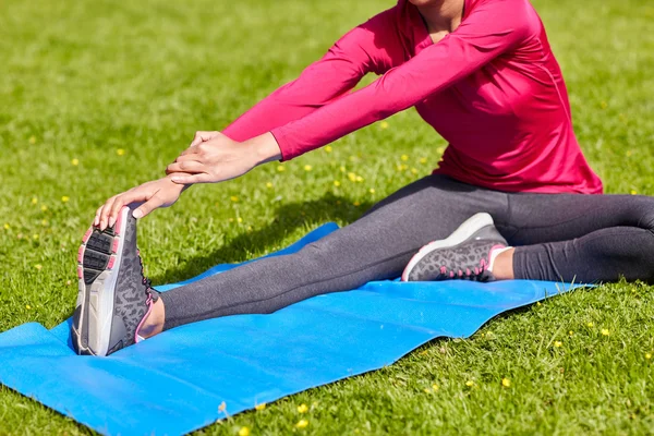 Primer plano de la mujer que estira la pierna en la estera al aire libre — Foto de Stock