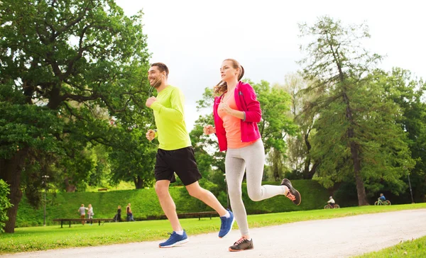 Smiling couple with earphones running outdoors — Stock Photo, Image