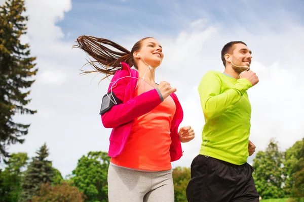 Smiling couple with earphones running outdoors — Stock Photo, Image