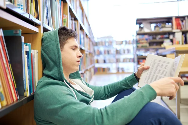 Student pojke eller ung man läsa bok i biblioteket — Stockfoto