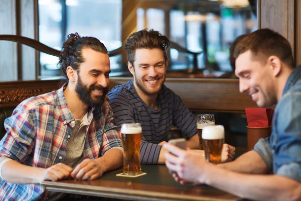 Друзья со смартфоном пьют пиво в баре — стоковое фото