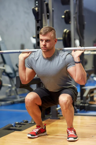 Jovem homem flexionando músculos com barbell no ginásio — Fotografia de Stock