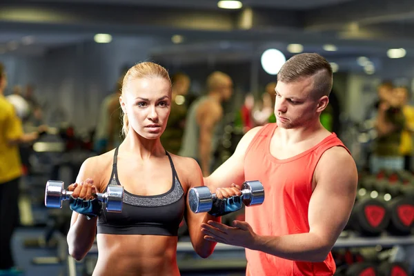 Pareja joven con mancuernas flexionando los músculos en el gimnasio — Foto de Stock