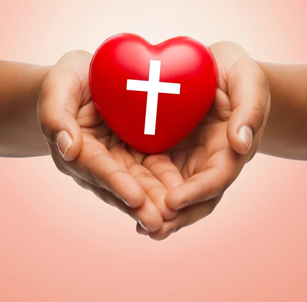 Close up of hands holding heart with cross symbol — Stock Photo, Image