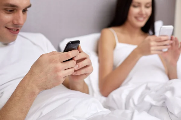 Primer plano de pareja sonriente en la cama con teléfonos inteligentes —  Fotos de Stock