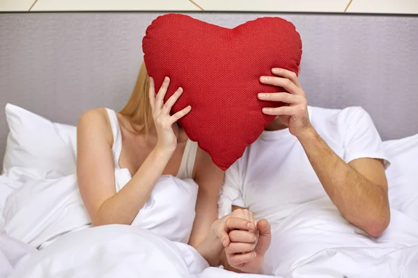 Счастливая пара в постели с красной подушкой в форме сердца — стоковое фото