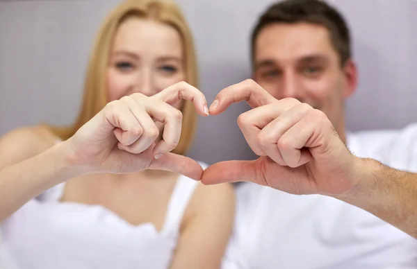 Sonriente pareja en cama haciendo corazón forma gesto — Foto de Stock