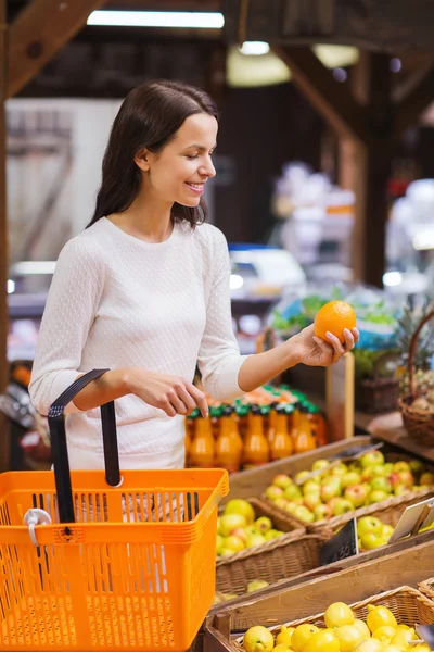 Gelukkig jonge vrouw met levensmiddelen mand in markt — Stockfoto