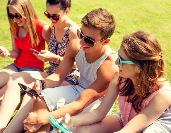 Lachende vrienden met smartphones zitten op gras — Stockfoto