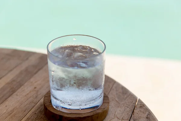 Стакан воды с кубиками льда на столе на пляже — стоковое фото