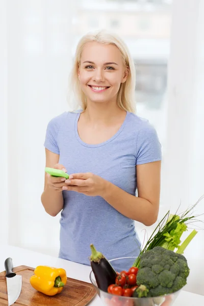 微笑与智能手机烹饪蔬菜的女士 — 图库照片