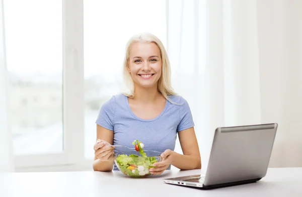 Uśmiechnięta kobieta jedzenie sałatka z laptopa w domu — Zdjęcie stockowe
