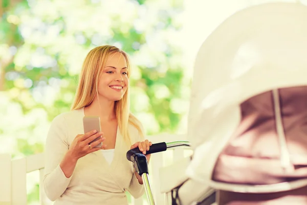 Madre feliz con smartphone y cochecito en el parque — Foto de Stock