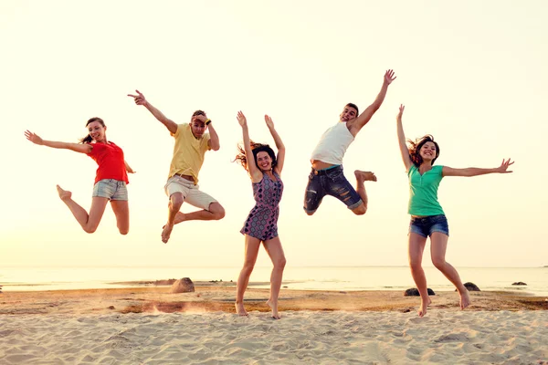 Amigos sonrientes bailando y saltando en la playa — Foto de Stock