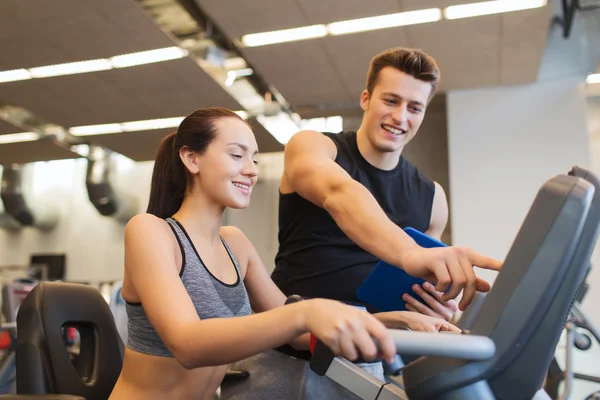 Glad kvinna med tränare på motionscykel i gym — Stockfoto