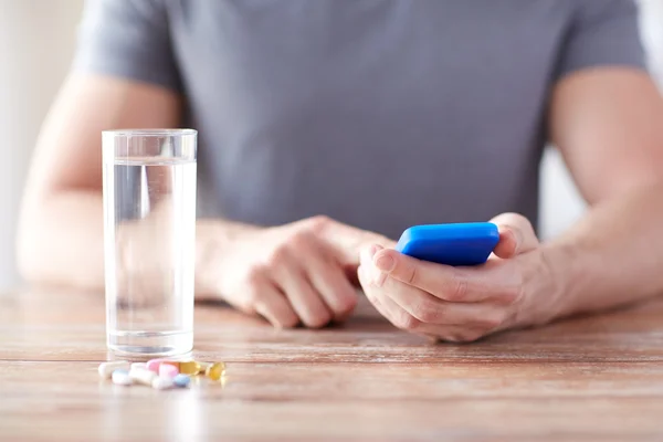 close up of hands with smartphone, pills and water