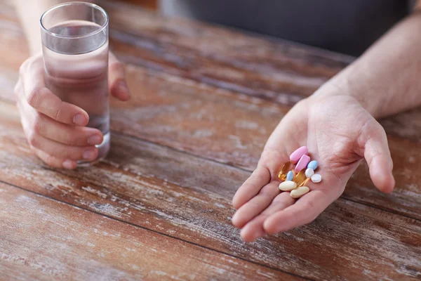 Close-up de mãos masculinas segurando pílulas e água — Fotografia de Stock