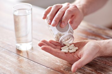 close up of man pouring pills from jar to hand clipart