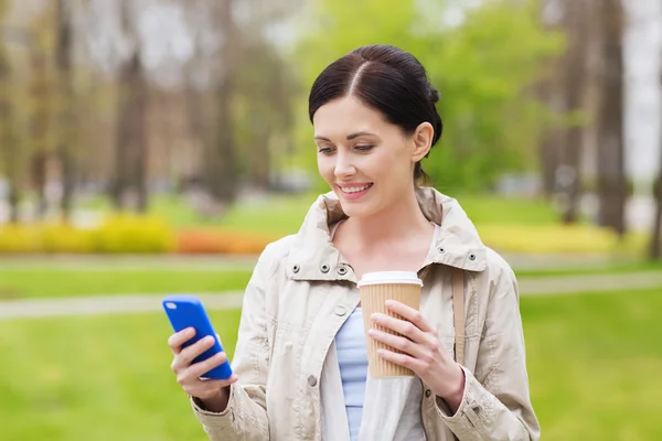 Mulher sorridente com smartphone e café no parque — Fotografia de Stock