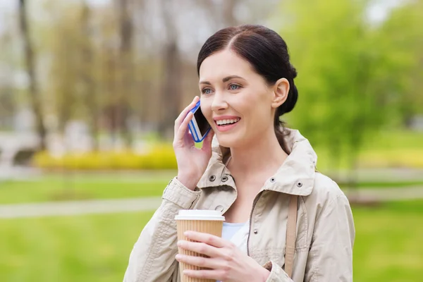 Donna sorridente con smartphone e caffè nel parco — Foto Stock