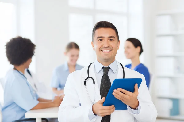 Счастливый врач с планшетным ПК над командой в клинике — стоковое фото