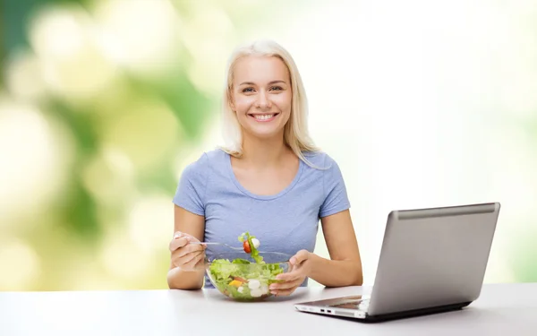 微笑的女人吃沙拉配笔记本电脑 — 图库照片