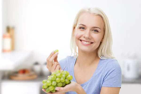 Mulher feliz comendo uvas na cozinha — Fotografia de Stock