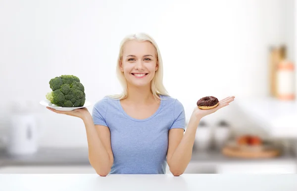 Smiling woman with broccoli and donut on kitchen Royalty Free Stock Photos