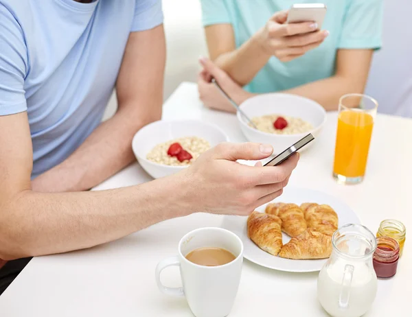 Close up of couple with smartphones at breakfast — Stock Photo, Image