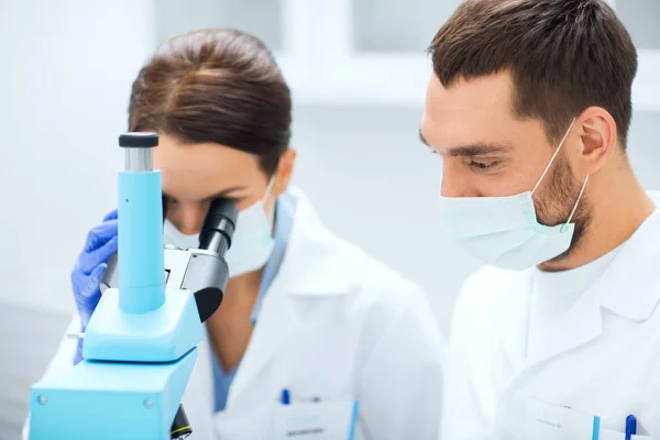 Científicos con máscaras mirando al microscopio en el laboratorio —  Fotos de Stock