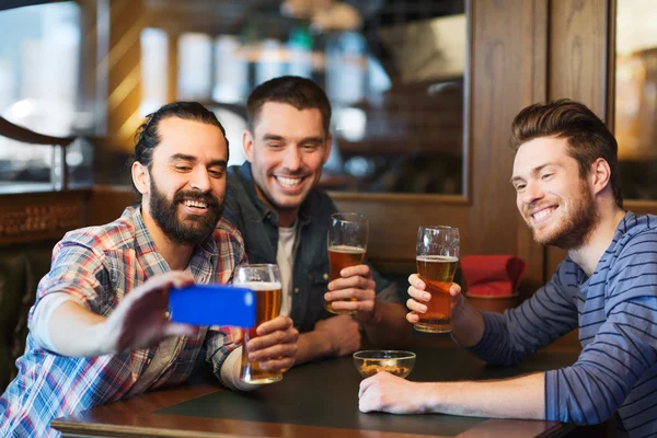 Amigos masculinos com smartphone bebendo cerveja no bar — Fotografia de Stock