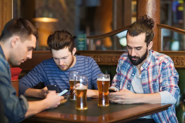 Manliga vänner med smartphones dricka öl på bar — Stockfoto