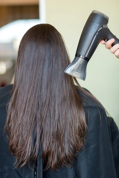 Main styliste avec ventilateur sèche les cheveux de la femme au salon — Photo