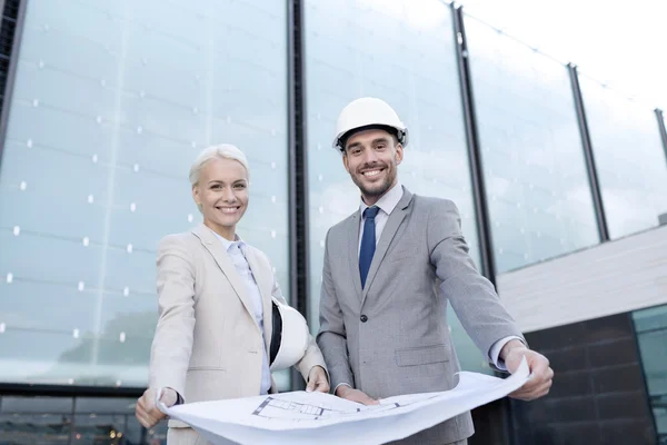 Glimlachende zakenmensen met blauwdruk en helmen — Stockfoto